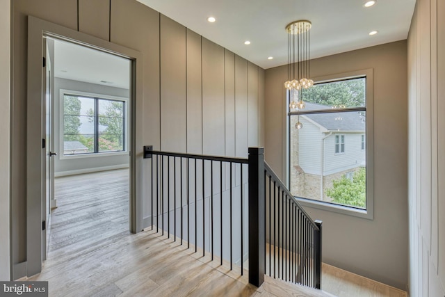 corridor with a notable chandelier, a healthy amount of sunlight, and light hardwood / wood-style floors