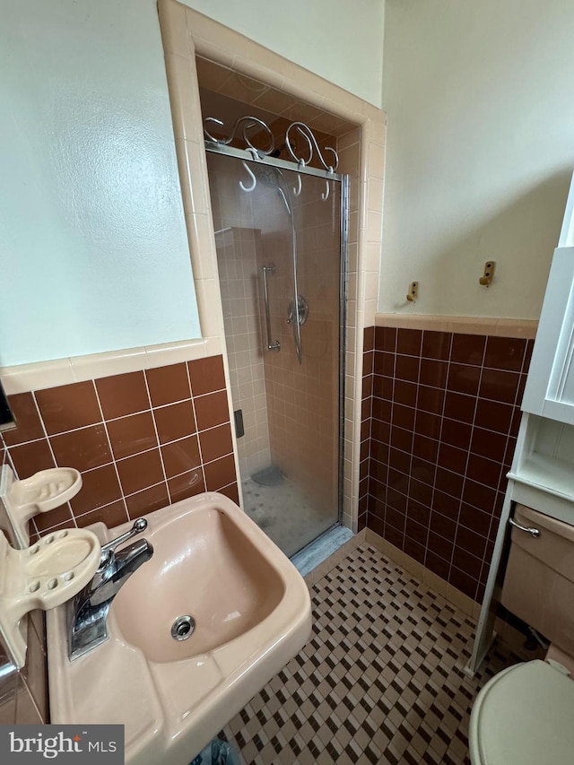 bathroom featuring sink, tile patterned floors, toilet, a shower with shower door, and tile walls