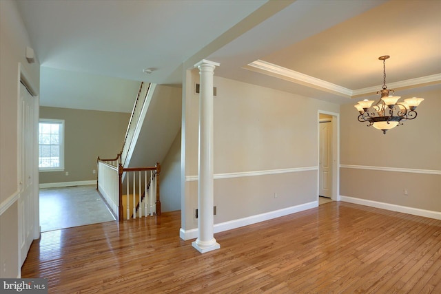 spare room with a notable chandelier, ornate columns, wood-type flooring, and a tray ceiling