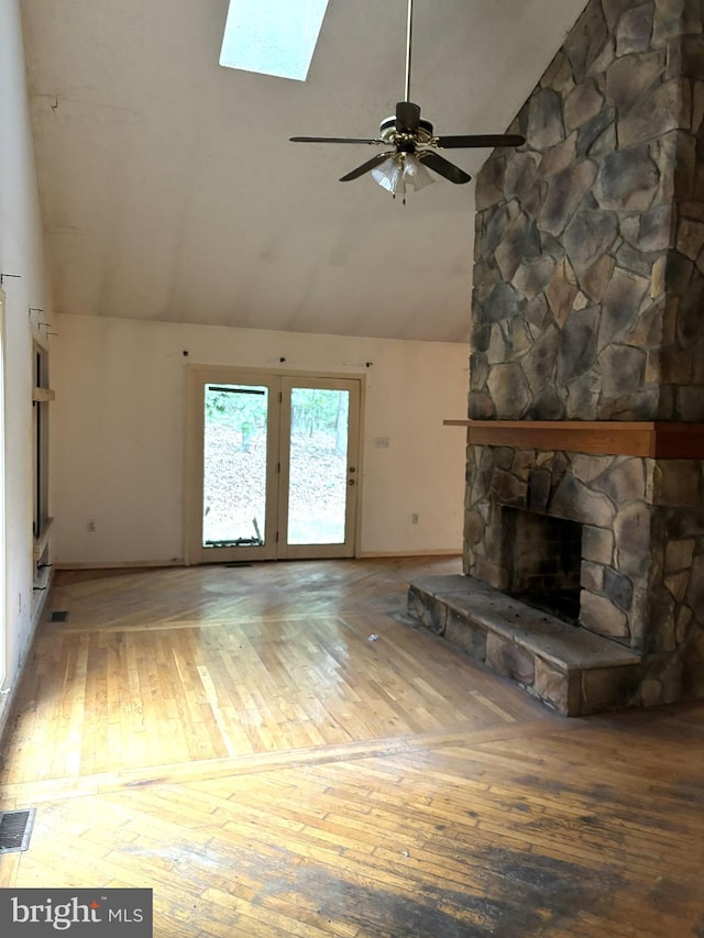 unfurnished living room featuring a stone fireplace, ceiling fan, vaulted ceiling with skylight, and wood-type flooring