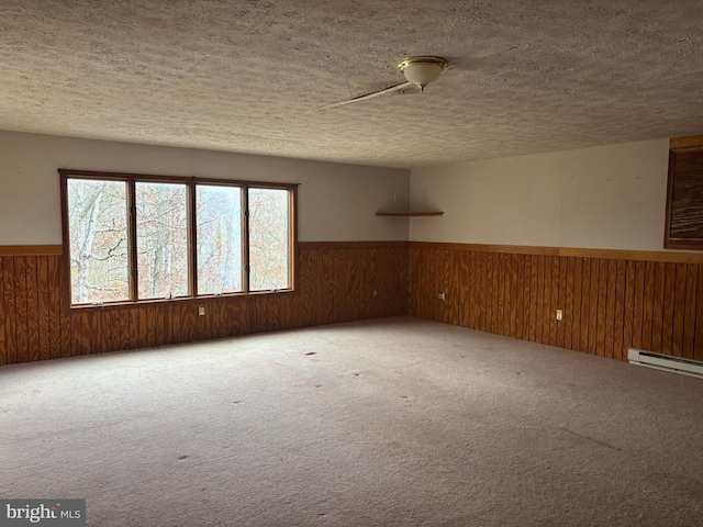 empty room with baseboard heating, wooden walls, carpet, and a textured ceiling