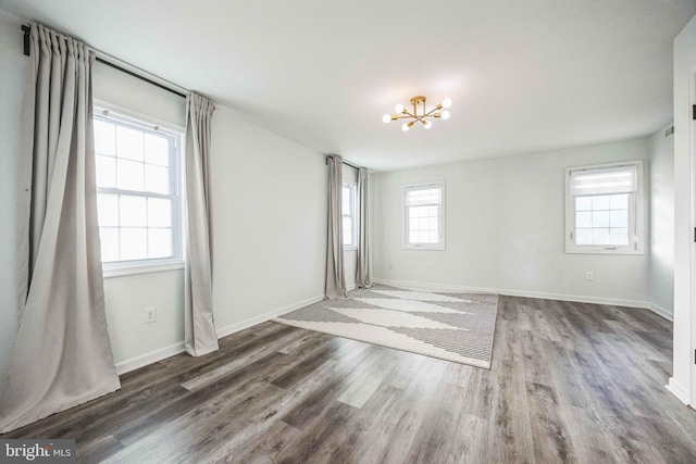 empty room featuring a notable chandelier, a healthy amount of sunlight, and wood-type flooring