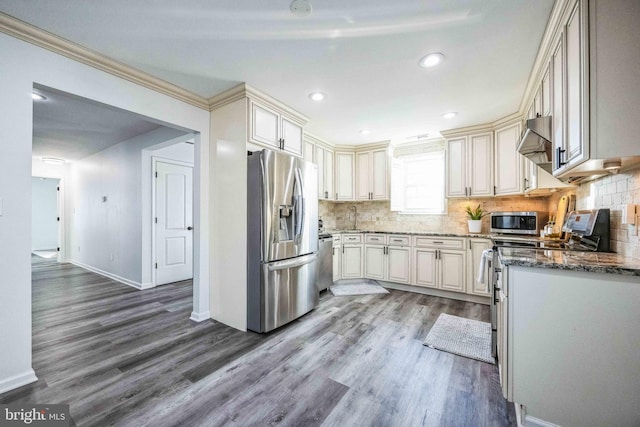 kitchen with appliances with stainless steel finishes, light wood-type flooring, wall chimney exhaust hood, crown molding, and stone counters