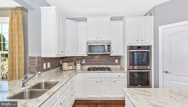 kitchen featuring light stone countertops, appliances with stainless steel finishes, tasteful backsplash, sink, and white cabinetry