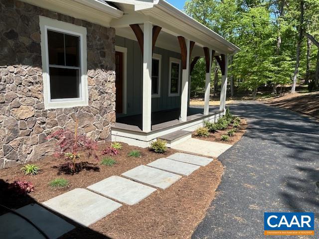 view of exterior entry featuring stone siding, a porch, and driveway