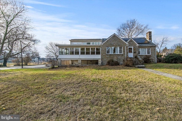 view of front facade featuring a sunroom, solar panels, and a front yard