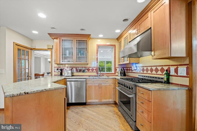 kitchen with sink, light wood-type flooring, appliances with stainless steel finishes, light stone counters, and kitchen peninsula