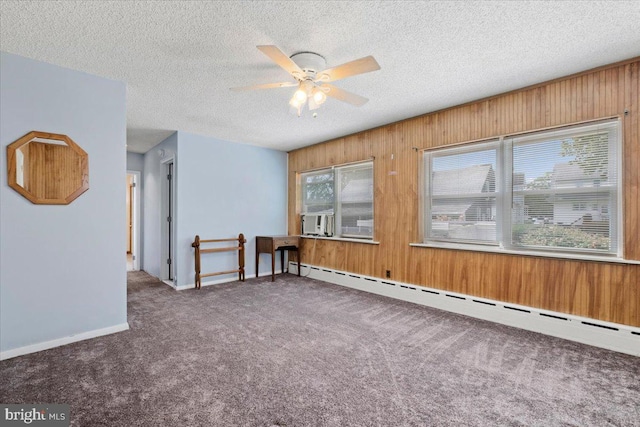 empty room with carpet flooring, ceiling fan, wooden walls, and a baseboard heating unit