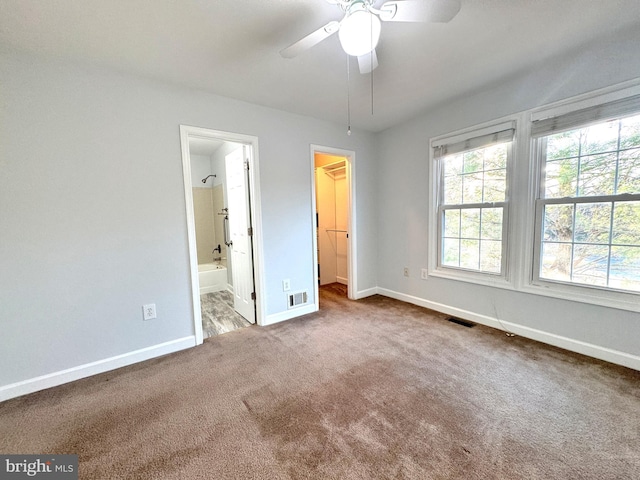 unfurnished bedroom featuring connected bathroom, ceiling fan, a walk in closet, a closet, and carpet