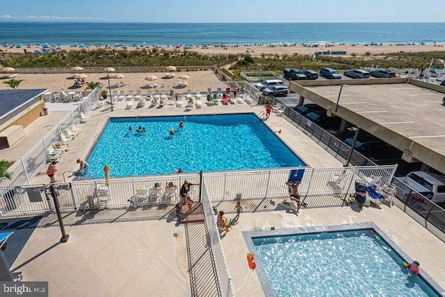 pool with a water view, fence, a beach view, and a patio