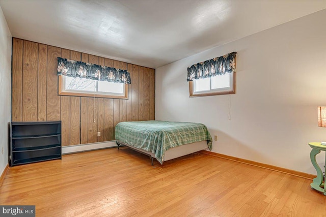 bedroom featuring light wood-type flooring, a baseboard radiator, multiple windows, and wooden walls