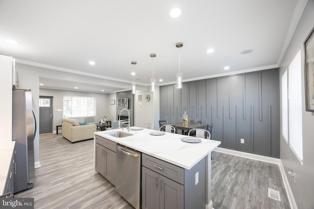 kitchen featuring light stone countertops, ornamental molding, stainless steel appliances, sink, and a center island with sink