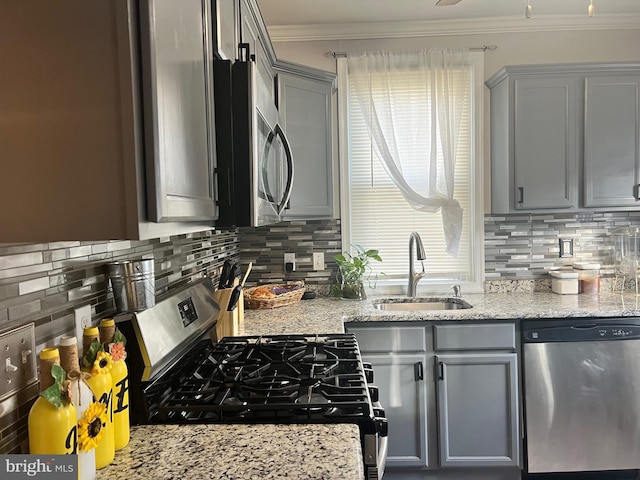 kitchen with gray cabinetry, crown molding, sink, appliances with stainless steel finishes, and light stone counters