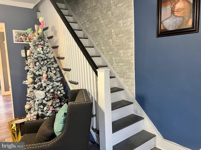 staircase with hardwood / wood-style floors, crown molding, and brick wall