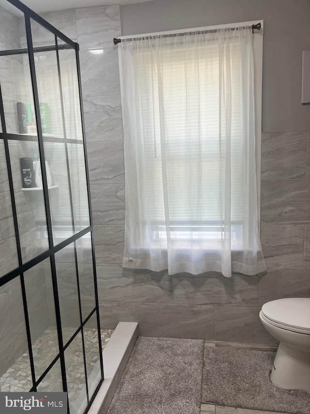 bathroom with toilet, a tile shower, and tile walls