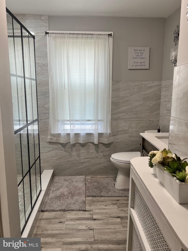 bathroom featuring a shower, vanity, toilet, and tile walls