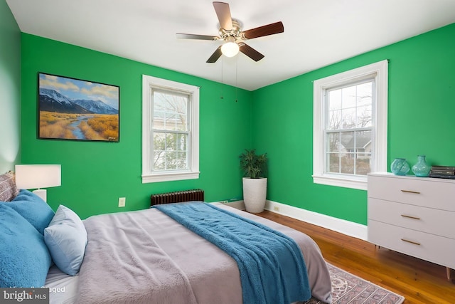 bedroom with hardwood / wood-style flooring, ceiling fan, radiator, and multiple windows