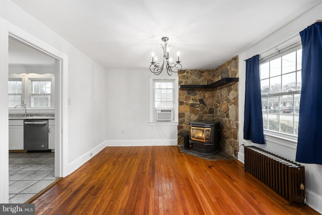 unfurnished living room with cooling unit, an inviting chandelier, light hardwood / wood-style flooring, radiator heating unit, and a wood stove