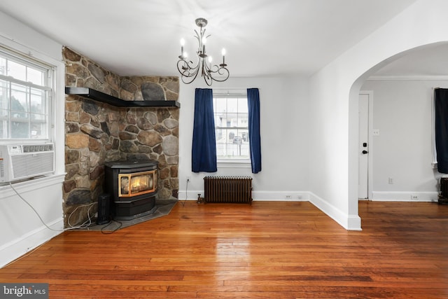 unfurnished living room featuring cooling unit, hardwood / wood-style floors, a chandelier, radiator heating unit, and a wood stove