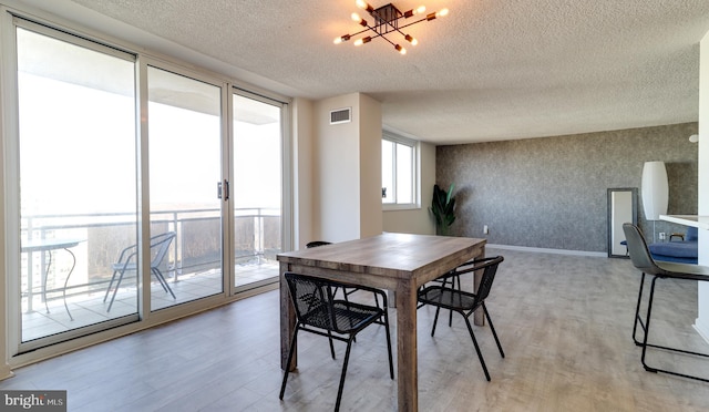 dining space with light hardwood / wood-style floors, a textured ceiling, and an inviting chandelier