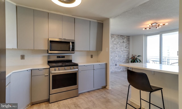 kitchen featuring gray cabinets, a kitchen bar, stainless steel appliances, and light hardwood / wood-style flooring