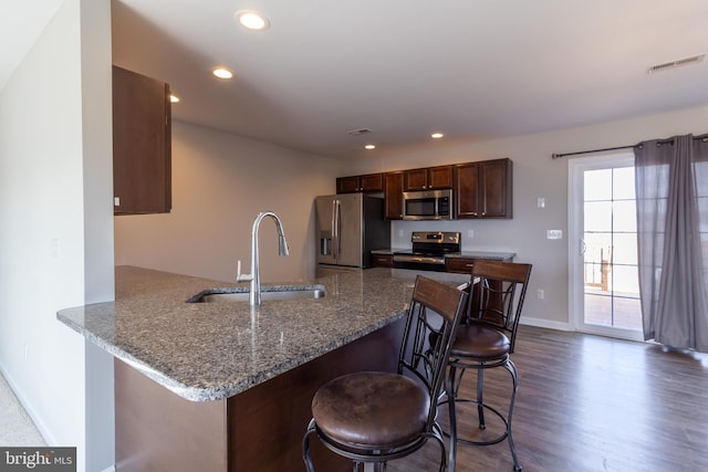 kitchen with sink, dark hardwood / wood-style floors, kitchen peninsula, a kitchen bar, and appliances with stainless steel finishes