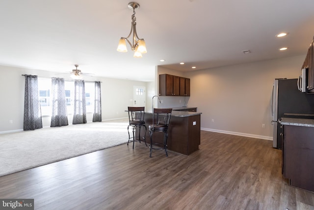 kitchen featuring a kitchen breakfast bar, dark hardwood / wood-style flooring, appliances with stainless steel finishes, ceiling fan with notable chandelier, and hanging light fixtures