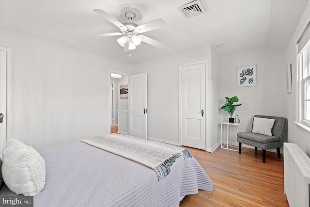 bedroom featuring ceiling fan, radiator heating unit, light hardwood / wood-style floors, and multiple windows