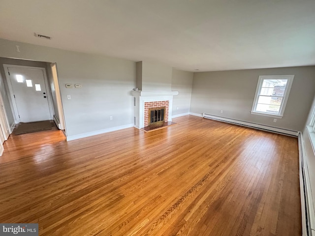 unfurnished living room featuring wood-type flooring, a brick fireplace, and baseboard heating