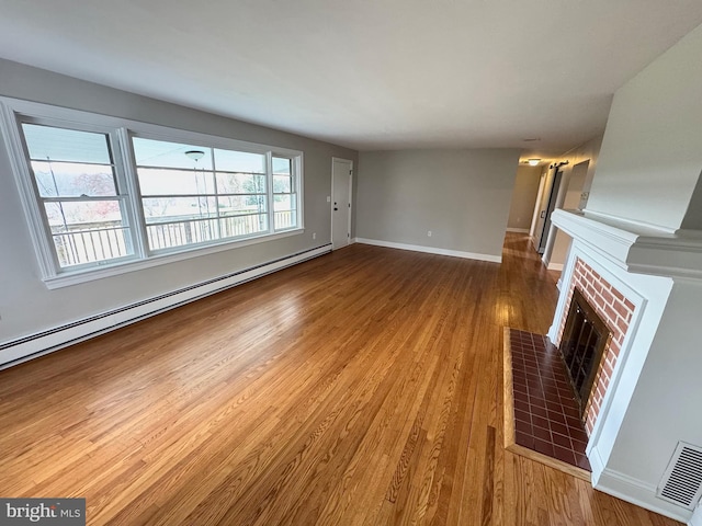 unfurnished living room featuring hardwood / wood-style floors, a brick fireplace, and a baseboard heating unit