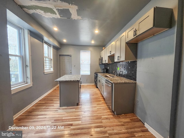 kitchen featuring light stone countertops, light hardwood / wood-style flooring, backsplash, a kitchen island, and appliances with stainless steel finishes