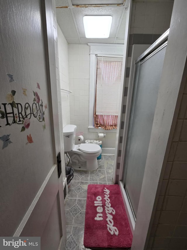 bathroom featuring toilet, a drop ceiling, tile walls, and walk in shower