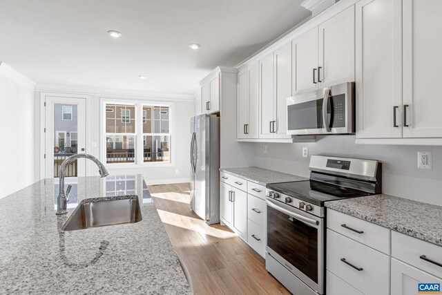 kitchen with white cabinets, sink, light wood-type flooring, ornamental molding, and appliances with stainless steel finishes