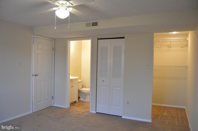 unfurnished bedroom with light carpet, ensuite bath, ceiling fan, and multiple closets