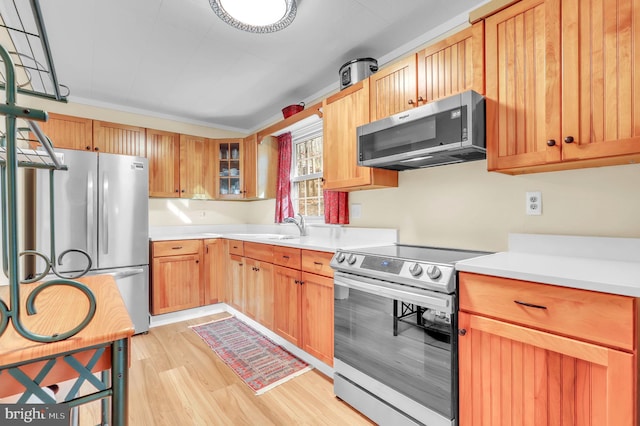 kitchen featuring appliances with stainless steel finishes, light hardwood / wood-style floors, crown molding, and sink