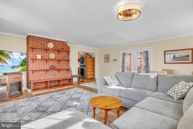 living room featuring a fireplace, stacked washer and dryer, light hardwood / wood-style floors, and ornamental molding