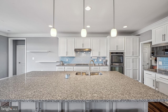 kitchen featuring pendant lighting, stainless steel double oven, a spacious island, and sink