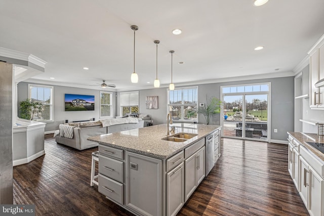 kitchen with ceiling fan, sink, hanging light fixtures, stainless steel dishwasher, and a kitchen island with sink