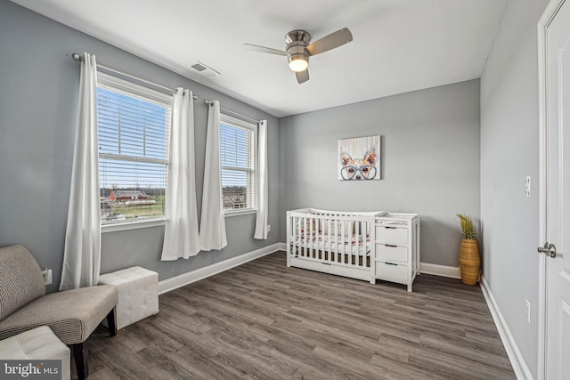 bedroom with ceiling fan, dark hardwood / wood-style flooring, and a nursery area