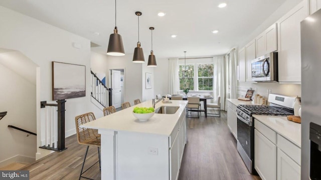 kitchen with pendant lighting, hardwood / wood-style floors, an island with sink, appliances with stainless steel finishes, and white cabinetry