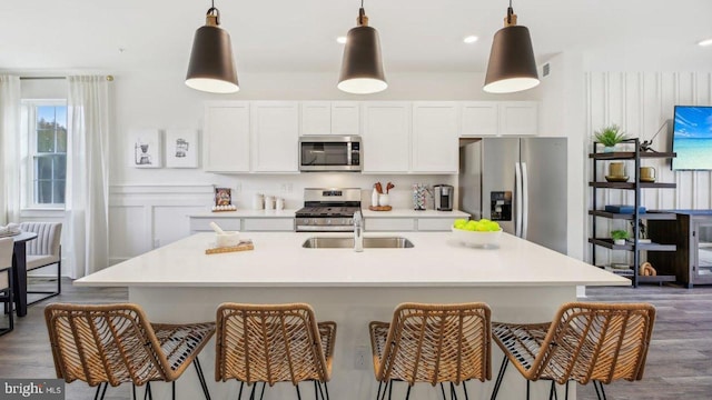 kitchen featuring a kitchen island with sink, dark wood-type flooring, stainless steel appliances, and decorative light fixtures