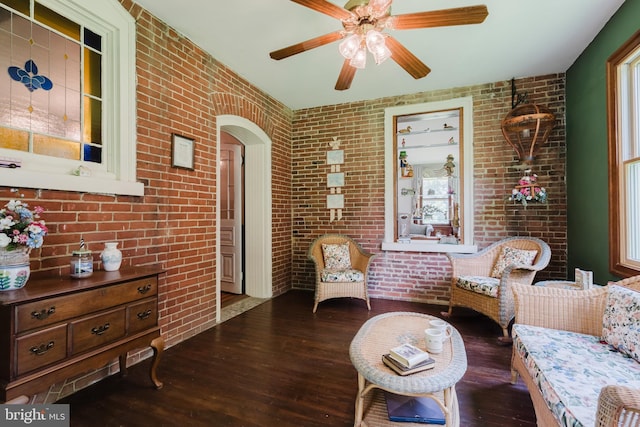 living room with a wealth of natural light, ceiling fan, dark wood-type flooring, and brick wall