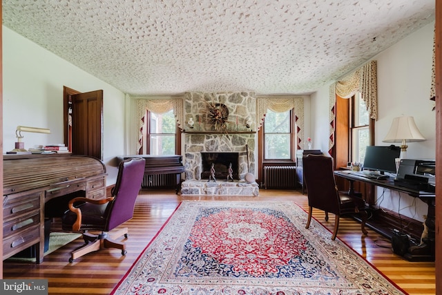 office with radiator, a healthy amount of sunlight, wood-type flooring, and a textured ceiling