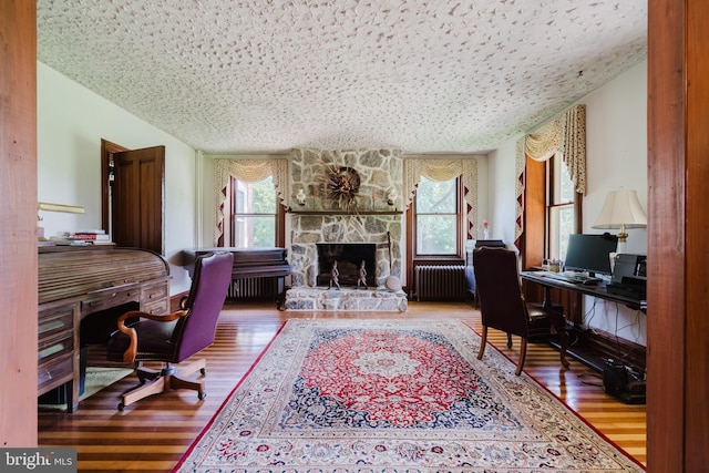 office space with radiator, a stone fireplace, a textured ceiling, and hardwood / wood-style flooring