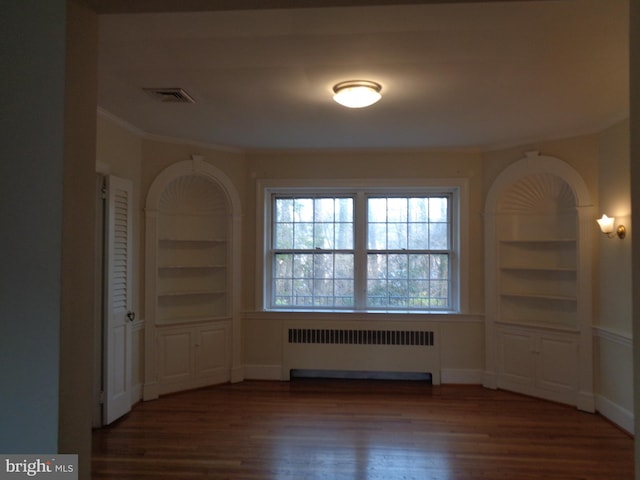 empty room featuring radiator heating unit, dark hardwood / wood-style floors, built in features, and ornamental molding