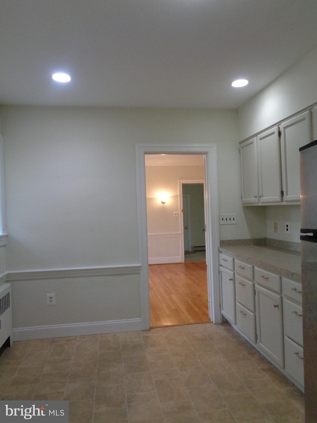 kitchen with white cabinets, radiator heating unit, light wood-type flooring, and stainless steel refrigerator