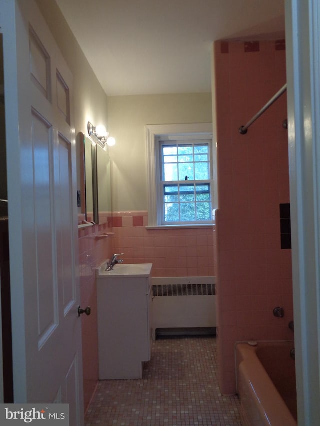 bathroom with radiator heating unit, tiled shower / bath combo, tile patterned floors, vanity, and tile walls