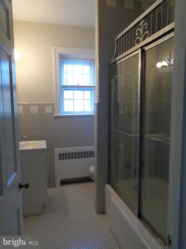 full bathroom with vanity, shower / bath combination with glass door, tile patterned flooring, tile walls, and radiator heating unit