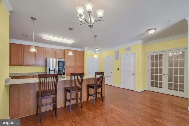 kitchen with french doors, stainless steel fridge with ice dispenser, crown molding, pendant lighting, and a kitchen bar