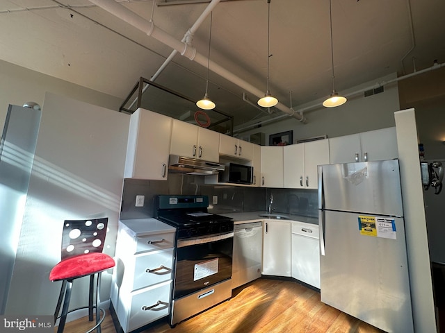 kitchen featuring decorative backsplash, white cabinets, hanging light fixtures, and appliances with stainless steel finishes